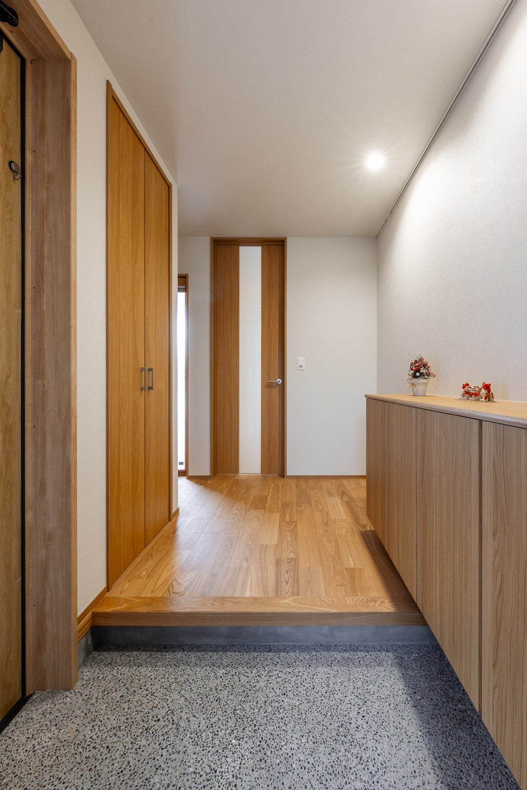 木目の床と建具に色味を合わせた巾木が見える玄関ホール